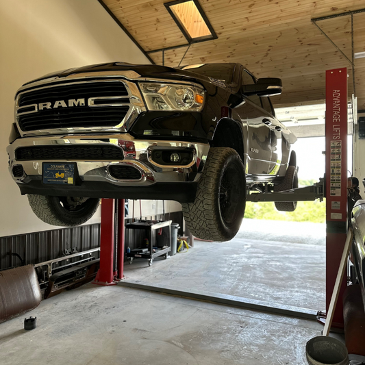 Advantage AL-12F 12,000 lbs 2-post lift raising black RAM truck in garage with wide post spacing and red columns
