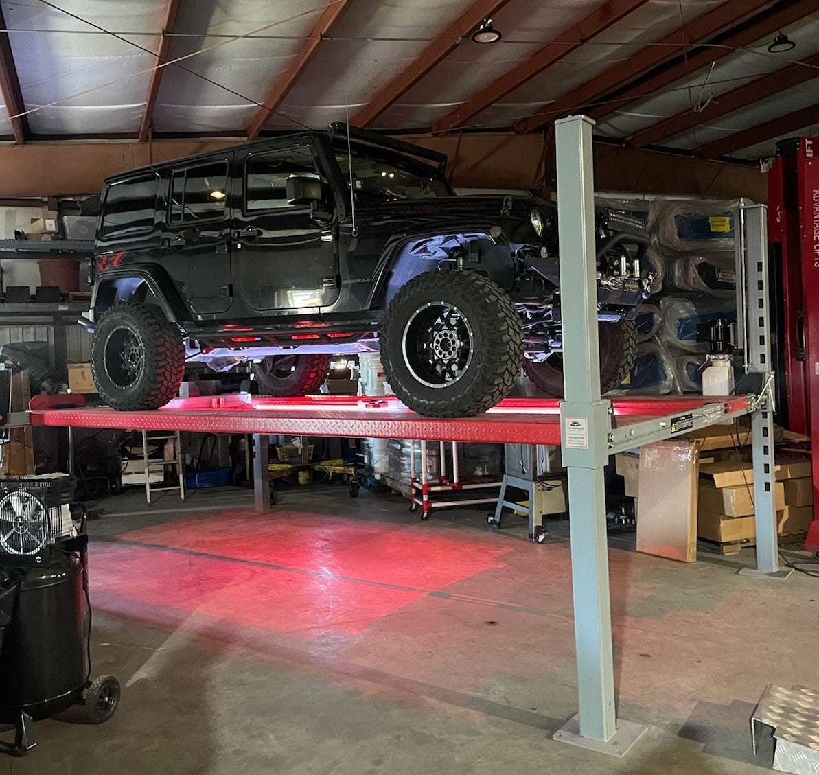Universal 4 post lift with magnetic LED lighting strip illuminating black off-road vehicle in garage