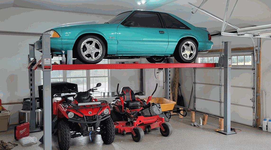 Advantage DX-9000-HD A turquoise car on top of a car lift with lawn mowers below it, taken inside a residential garage