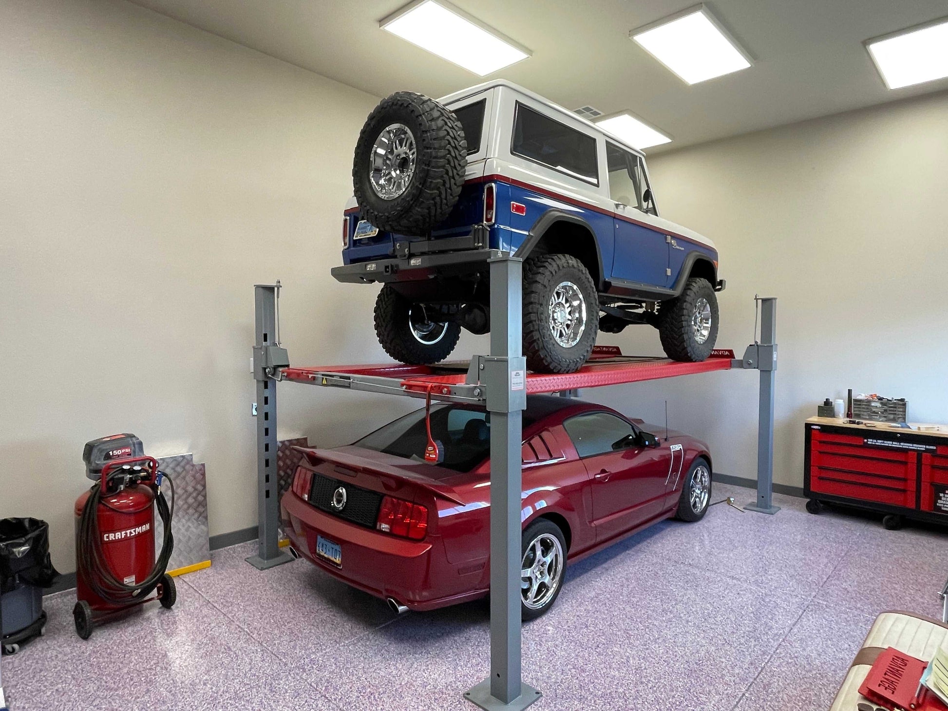 Advantage DX-9000-HD An old bronco on top of a car lift with a red sports car under it - taken inside a garage.
