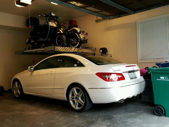 Single-post vehicle lift holding both a motorcycle and a moped over a Mercedes for extra space in a home garage