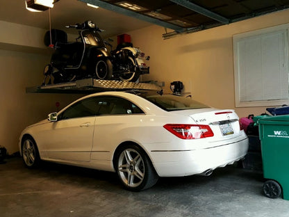 Single-post vehicle lift holding both a motorcycle and a moped over a Mercedes for extra space in a home garage